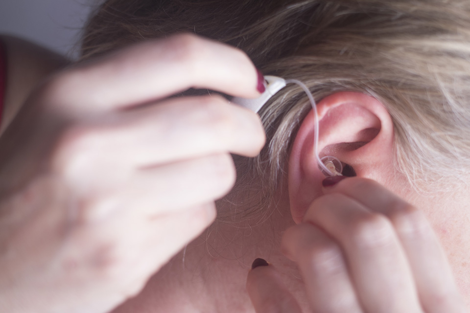 Adult woman putting hearing aid in her ear